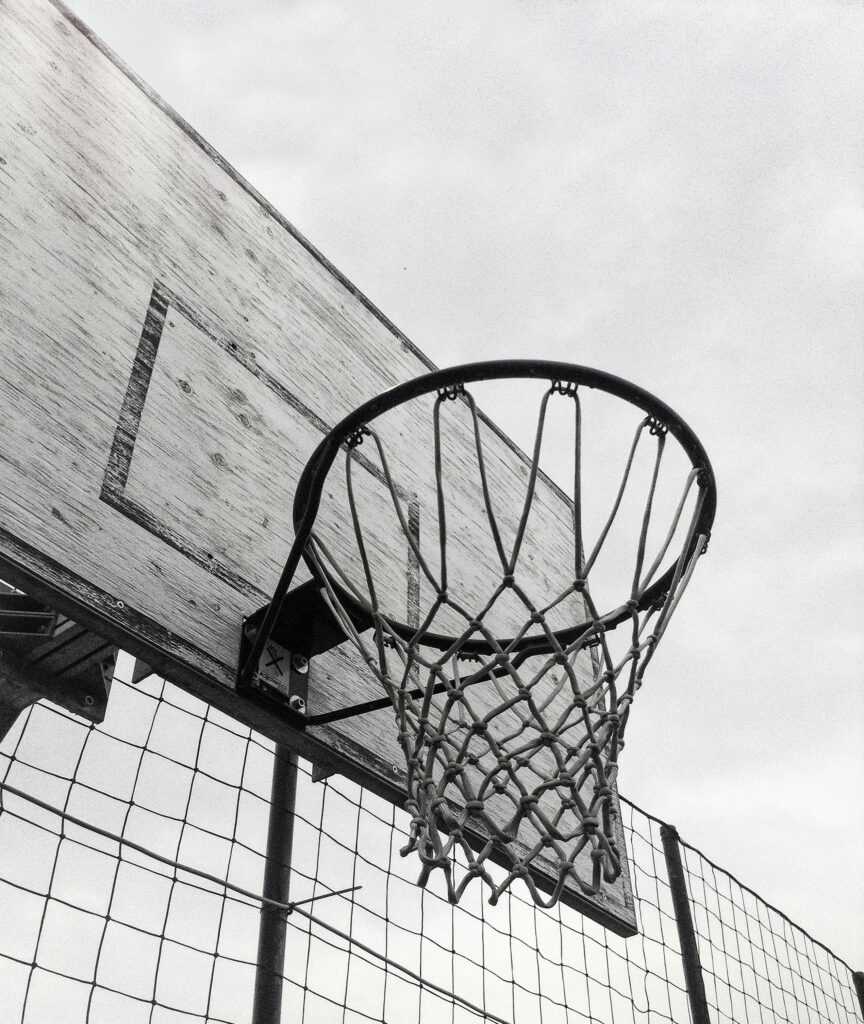 Monochrome shot of a basketball hoop against the sky, capturing the essence of outdoor sports.
