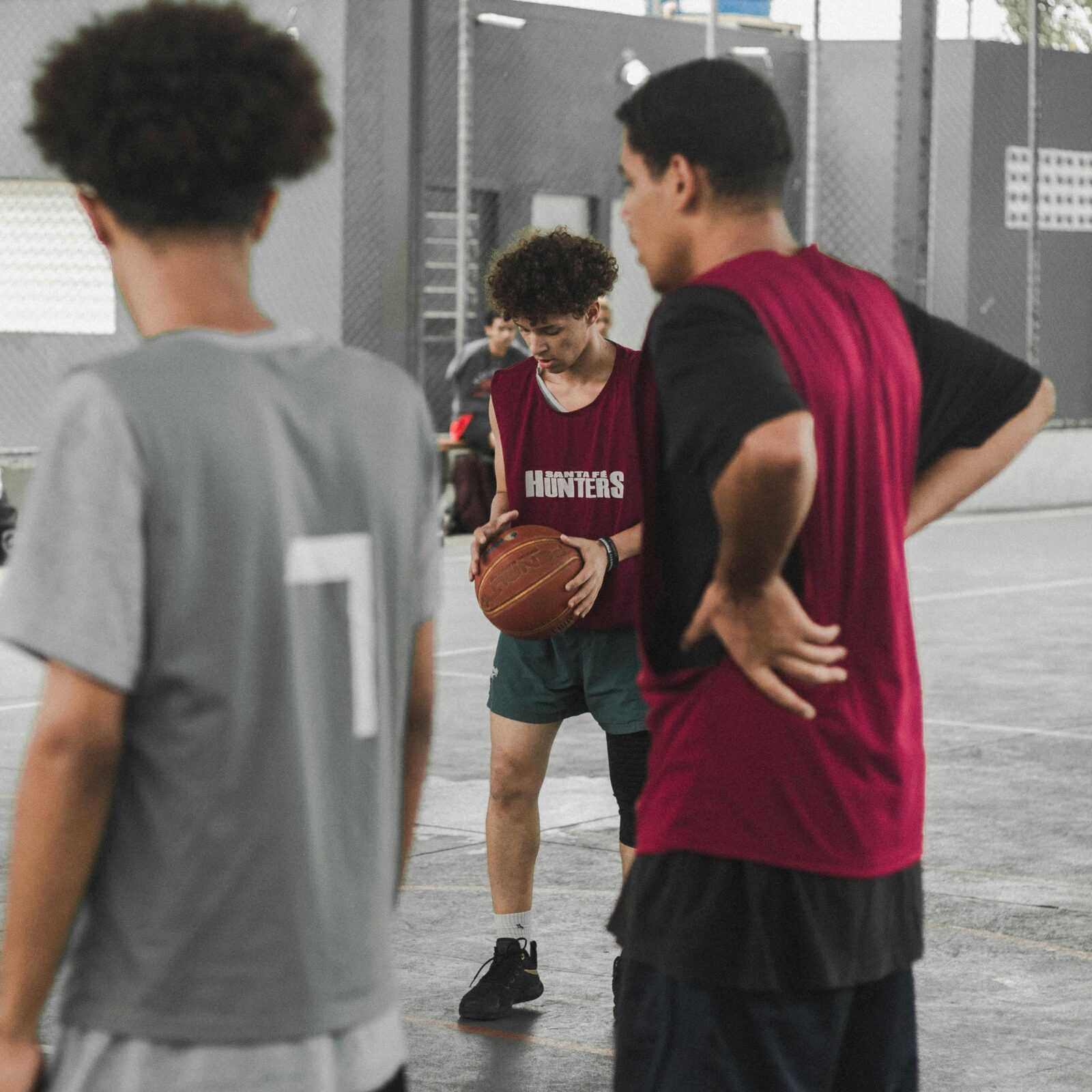 A group of teenagers playing basketball indoors, focusing on a player holding the ball during practice.