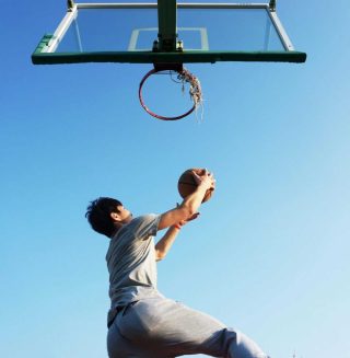 A young man jumping to dunk a basketball outdoors in clear daylight.